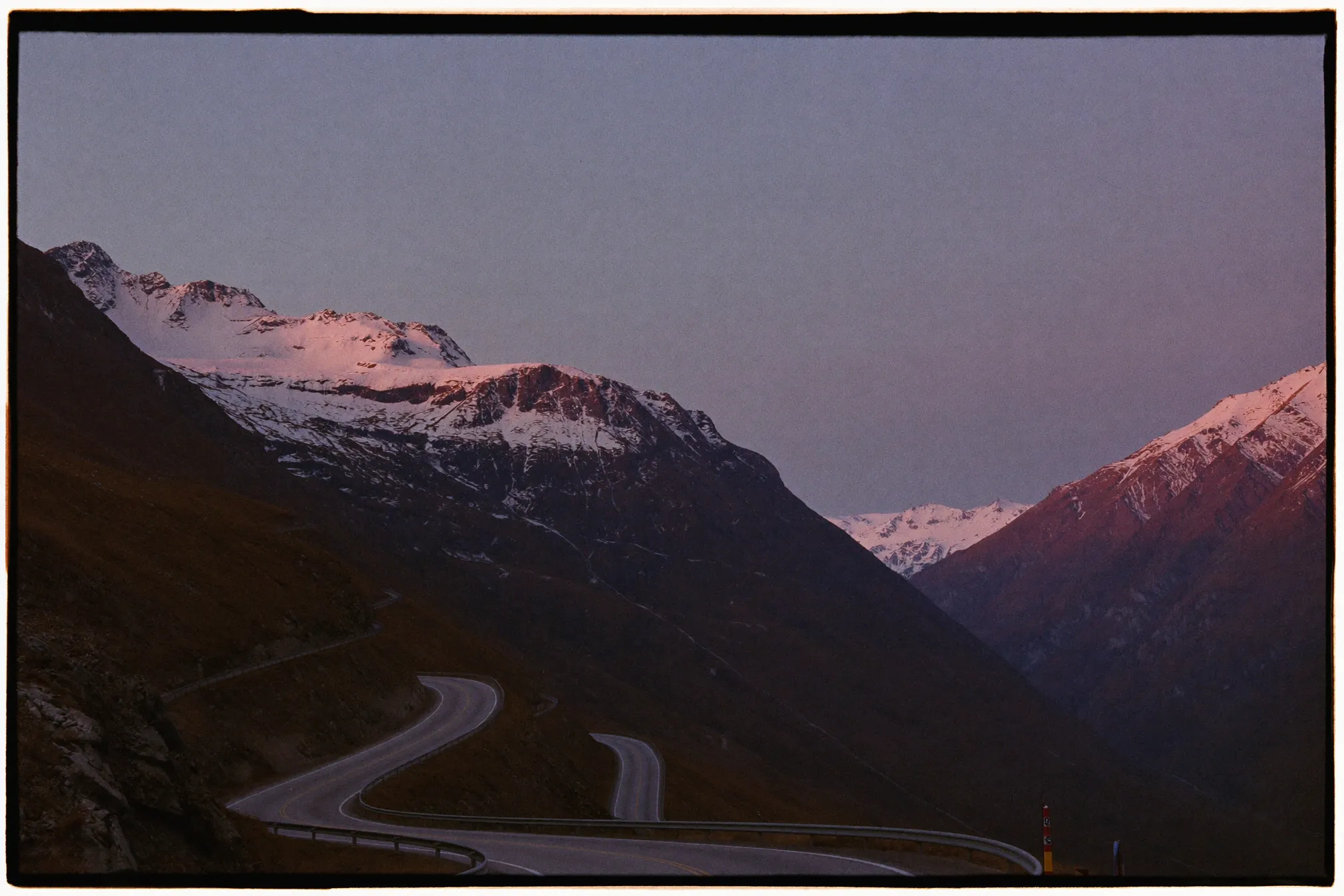 Mountain pass road with hairpin switchbacks climbing an alpine valley at dusk under a violet sky